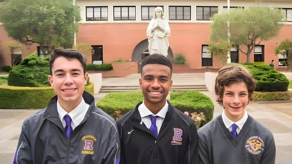 Tres estudiantes en uniformes escolares están frente a una estatua en el campus de la Archbishop Riordan High School.