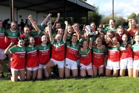 Un grupo de jóvenes atletas de Ardscoil Phadraig celebra juntas en un campo de hierba.