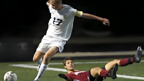 Un jugador de fútbol con camiseta blanca salta sobre un jugador con camiseta roja en el campo de Arlington High School.