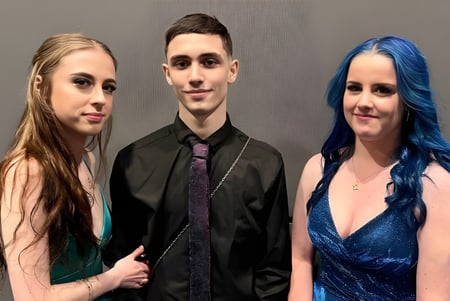 Tres personas posan juntas frente a un fondo gris en una foto de equipo de la Armadale Senior High School.