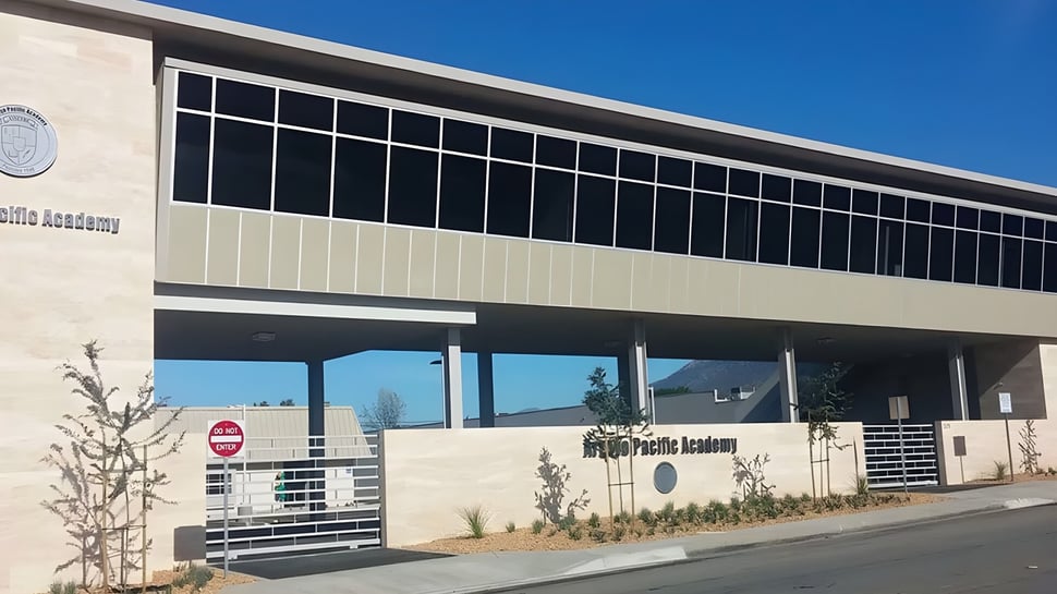 El moderno edificio principal de varios pisos de la Arroyo Pacific Academy con grandes ventanas frente a un cielo azul claro.