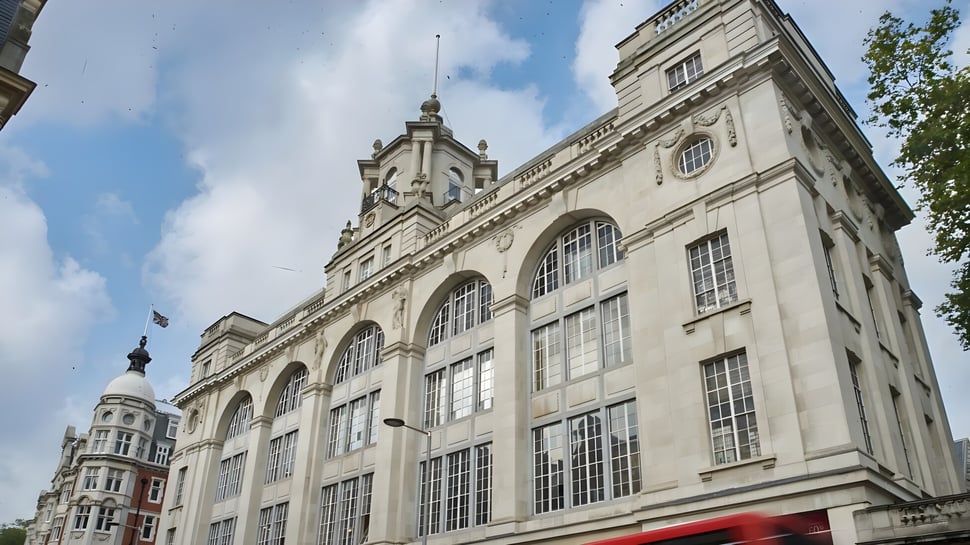 El edificio principal con reloj y ventanas de arco en el campus del Ashbourne College está rodeado de árboles.