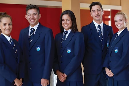 Un grupo de estudiantes en uniformes azules está junto a Ashdale Secondary College frente a una pared roja.