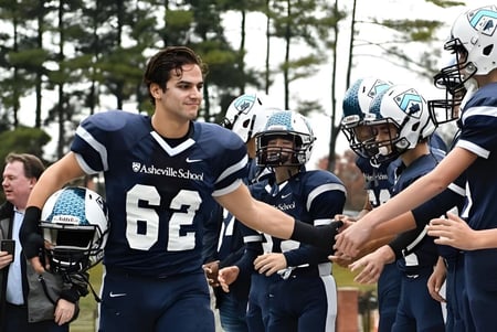 Un grupo de jugadores de fútbol de la Asheville School se saluda en un campo de juego con árboles.