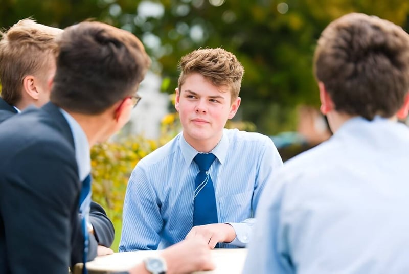 Un grupo de alumnos de la Ashford School conversa frente a un fondo verde y florido.