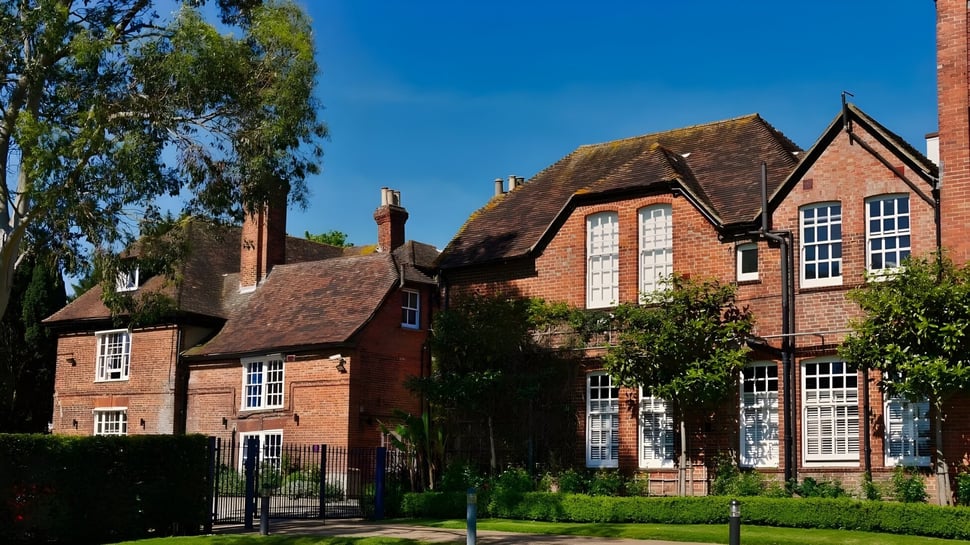 El edificio de ladrillo de la Ashford School con techo de paja está rodeado de áreas verdes bajo un cielo despejado.