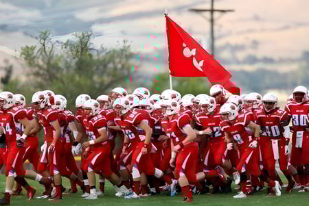 Un grupo de futbolistas en uniformes rojos con una bandera roja en el campo de deportes del Ashland School District.