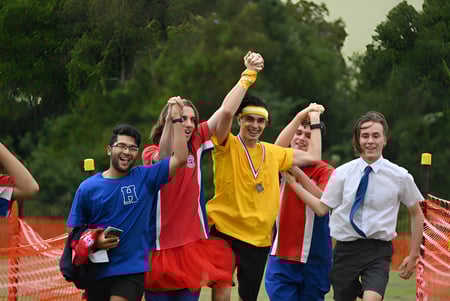 Un grupo de estudiantes celebrando levanta los brazos en el parque del campus de la Aspley State High School.