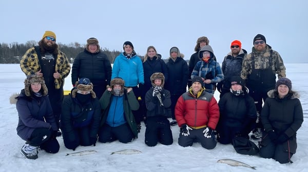 Estudiantes de Assumption College Catholic High School están vestidos para el invierno en un campo nevado frente a un bosque.