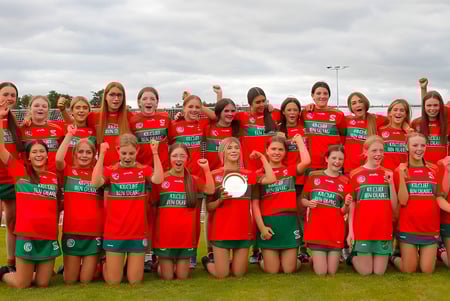 Un grupo de jóvenes futbolistas está en el campo de deportes de la Assumption Grammar School bajo un cielo nublado.