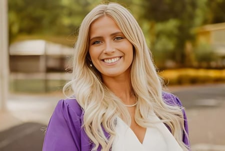 Una mujer sonríe frente a un área exterior borrosa en el campus de la Athens Christian School.