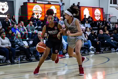 Dos alumnas del Athlete Institute juegan baloncesto en la cancha frente a los espectadores.