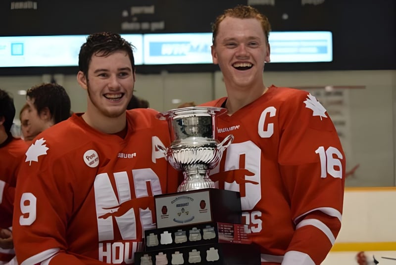 Dos jugadores de hockey del Athol Murray College of Notre Dame celebran su victoria con un trofeo sobre el hielo.