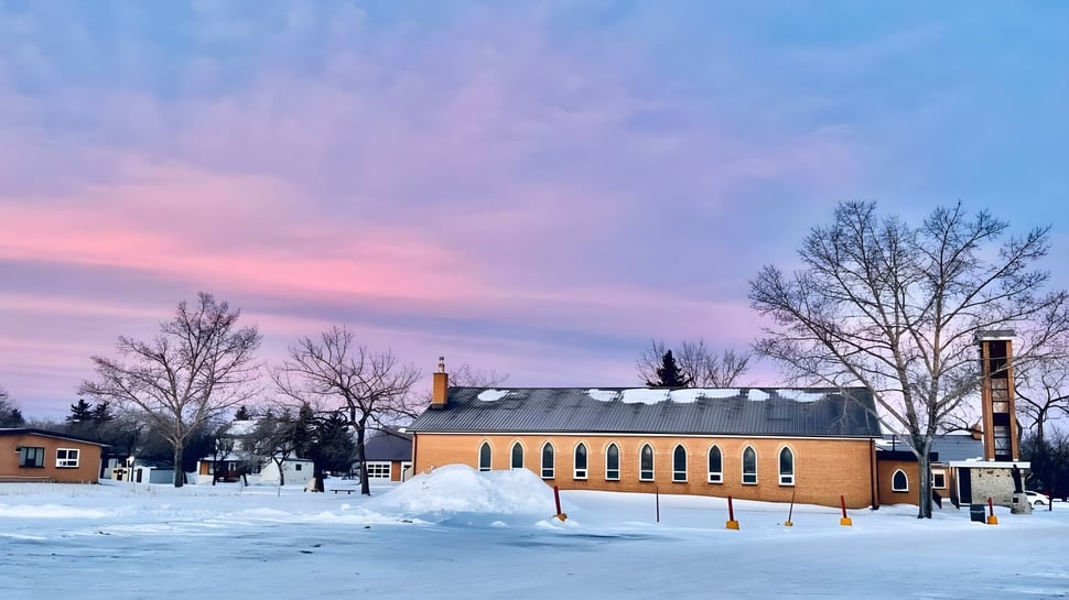 El Athol Murray College of Notre Dame muestra un edificio de ladrillo con un bosque invernal nevado y un cielo colorido de fondo.