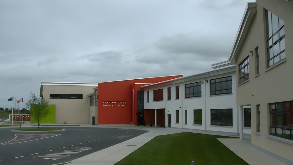 El moderno edificio de varios pisos con pared de acento roja en el campus del Athy College está rodeado de un área pavimentada y una superficie de césped.
