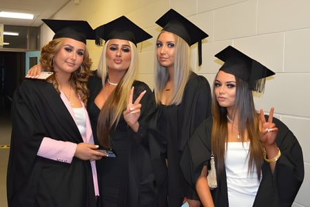 Cuatro estudiantes en ropa de graduación posan juntas en el pasillo del Athy College.