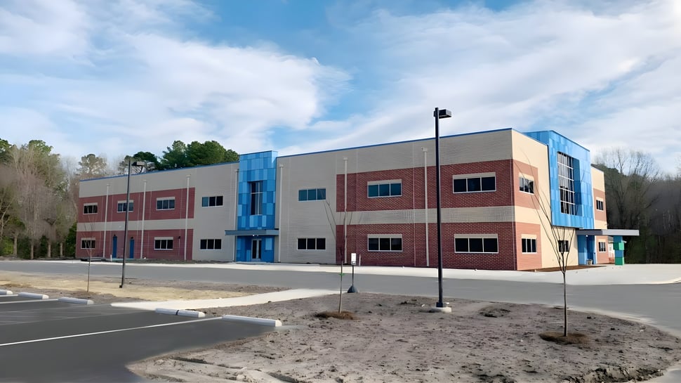 El moderno edificio de varios pisos de la Atlantic Shores Christian School está rodeado de árboles y un cielo despejado.