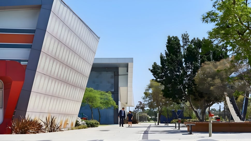 El moderno edificio del Atwell College está rodeado de instalaciones verdes y se encuentra frente a un claro cielo azul.