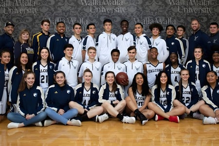Un grupo de jóvenes atletas en el centro deportivo de la Auburn Adventist Academy posan juntos frente al logo.