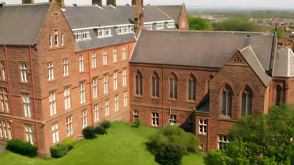El edificio de la Austin Friars School con un paisaje verde en primer plano y la ciudad de fondo.