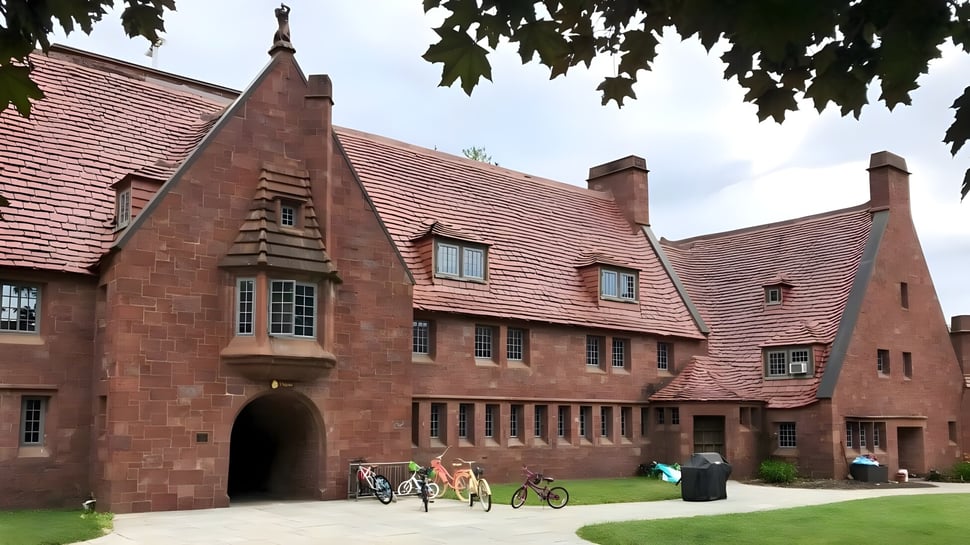 El histórico edificio de ladrillo con techo de tejas rojas de la Avon Old Farms School está rodeado de árboles y ciclistas.