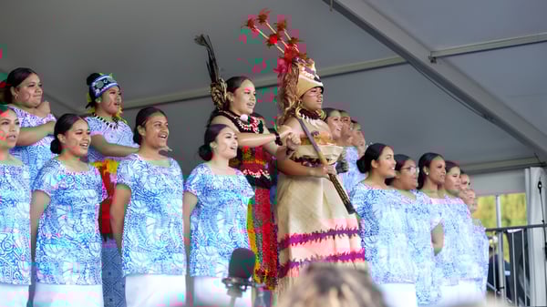 Alumnas de la Avonside Girls' High School realizan una actuación con vestimenta tradicional hawaiana en un escenario frente a una pared gris.