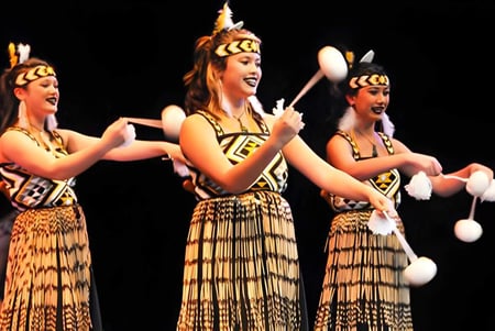 Tres estudiantes del Awatapu College realizan una danza étnica tradicional en un escenario.