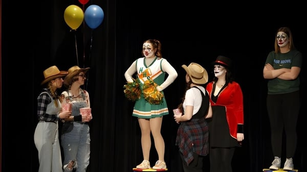 Un grupo de estudiantes del Baccalieu Collegiate está en trajes coloridos en un escenario con globos de fondo.