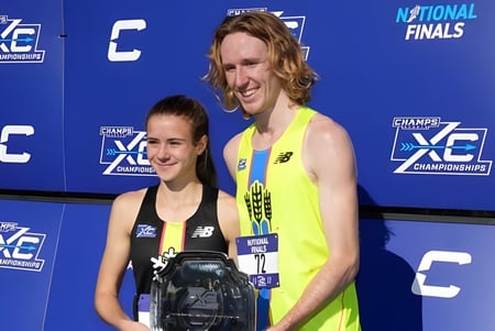 Dos atletas están frente al banner de los Campeonatos Nacionales de XC en el campus del Baccalieu Collegiate.