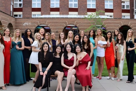 Un grupo de jóvenes mujeres vestidas de manera formal está frente a un edificio de ladrillo con ventanas de arco en el terreno de la Badminton School.