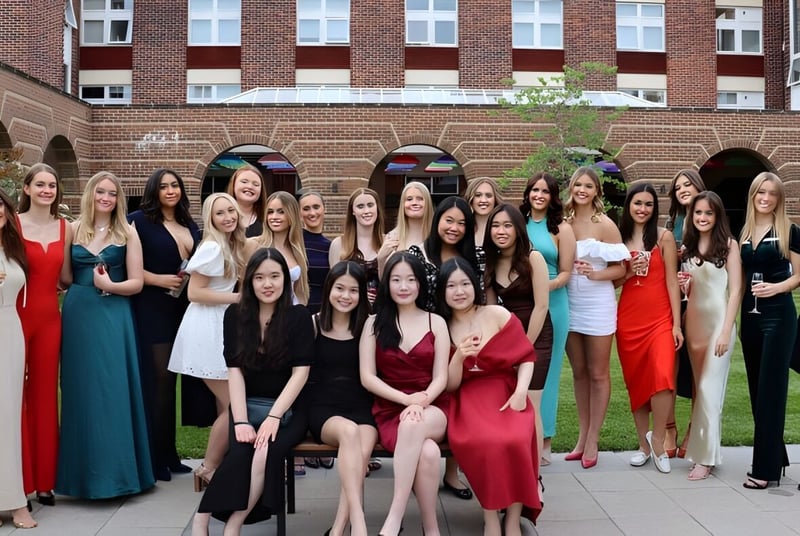 Un grupo de jóvenes mujeres vestidas de manera formal está frente a un edificio de ladrillo con ventanas de arco en el terreno de la Badminton School.