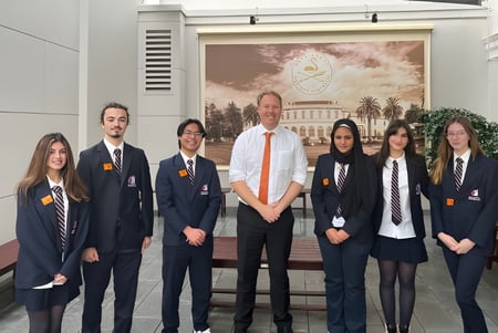 Un grupo de estudiantes en uniformes escolares está frente a un gran mural con una vista de la ciudad en el campus de la Balcatta Senior High School.