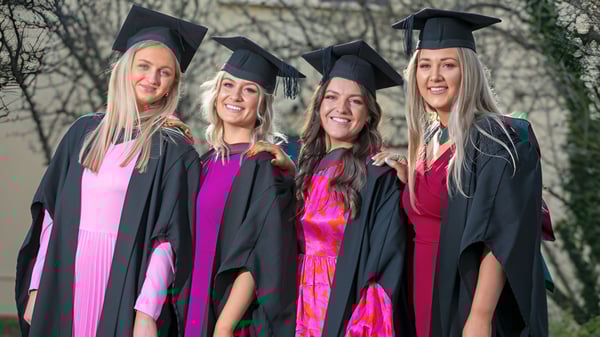 Cuatro graduadas de la Balla Secondary School están juntas al aire libre en sus togas de graduación.