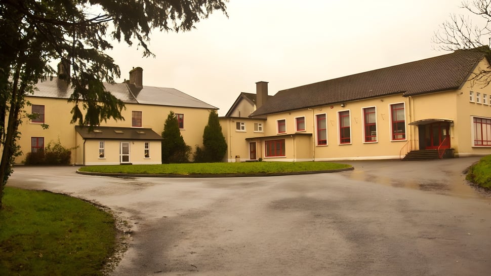 Una vista del pueblo con edificios amarillos y un camino de grava en el terreno de la Balla Secondary School.