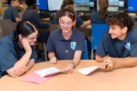 Tres estudiantes del Ballajura Community College están sentados en una mesa y trabajan juntos en una tarea de aprendizaje en el aula.