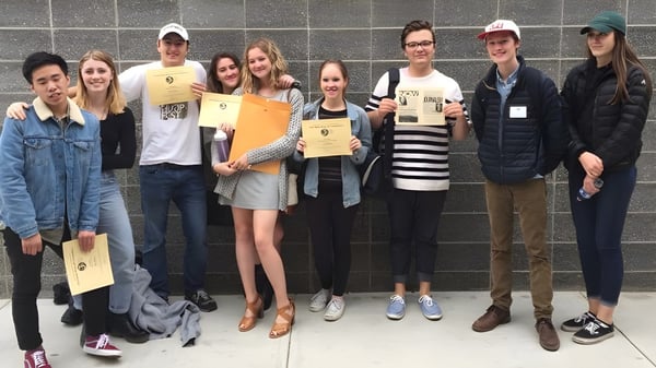 Un grupo de estudiantes de la Ballard High School está frente a una pared de azulejos sosteniendo certificados.