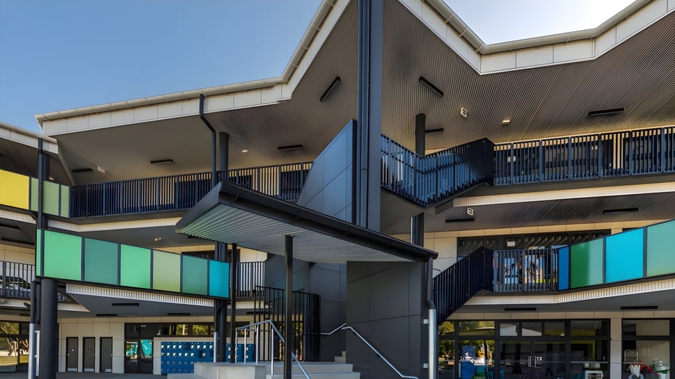 El colorido y moderno edificio escolar de la Ballina Coast High School con balcones y escaleras frente a un cielo azul.