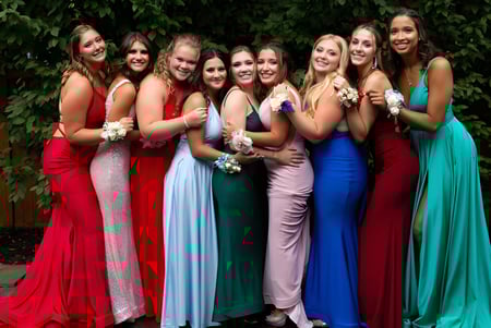 Un grupo de jóvenes alumnas de la Ballingarry Presentation School está al aire libre en un prado verde con vestidos formales coloridos.