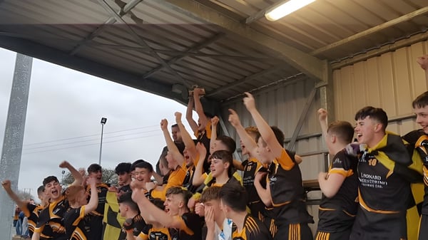 Estudiantes del Ballybay Community College levantan los brazos en una celebración conjunta en un gimnasio.