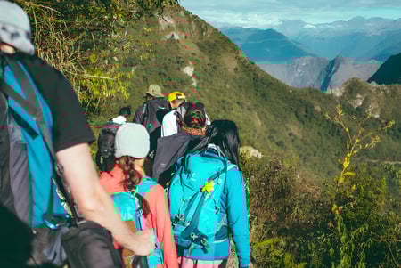 Un grupo de estudiantes del Ballybay Community College camina por un estrecho sendero de montaña con un impresionante paisaje montañoso de fondo.