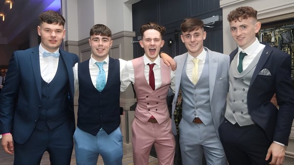 Un grupo de estudiantes del Banagher College posan en un evento formal frente a un fondo oscuro con iluminación de escenario.