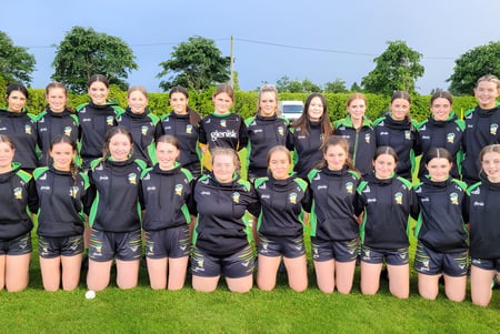 Un grupo de jóvenes futbolistas está en el campo deportivo del Banagher College frente a árboles y un cielo despejado.