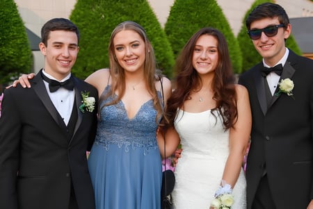 Cuatro jóvenes adultos de la Bandon Grammar School posan juntos en un jardín con plantas verdes y flores.