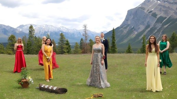 Un grupo de estudiantes está de pie en vestidos coloridos en una pradera frente a montañas en el terreno de la Banff Community High School.