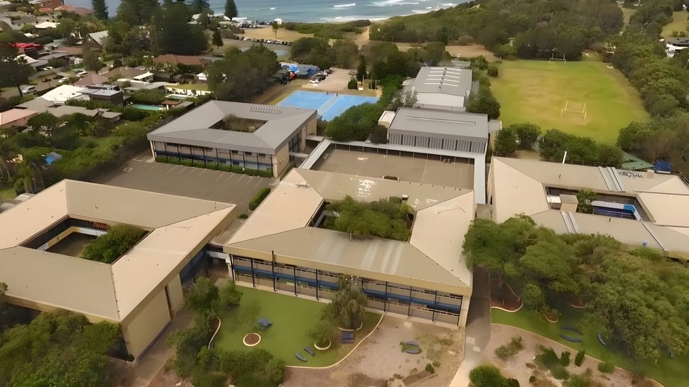 El moderno complejo de edificios de Barrenjoey High School está rodeado de naturaleza verde y muestra un área exterior con piscina.