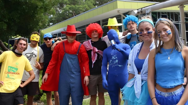 Un grupo de estudiantes de Barrenjoey High School lleva disfraces coloridos y está afuera frente a árboles y edificios.