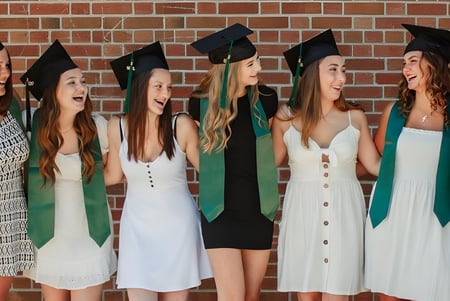 Un grupo de estudiantes en vestimenta de graduación se encuentra frente a una pared de ladrillo en el campus del Barrie North Collegiate Institute y celebra su graduación.