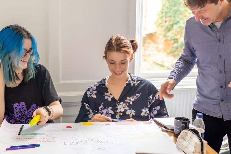 Estudiantes de la Bath Academy trabajan juntos en un proyecto de arte con diferentes materiales en la mesa.
