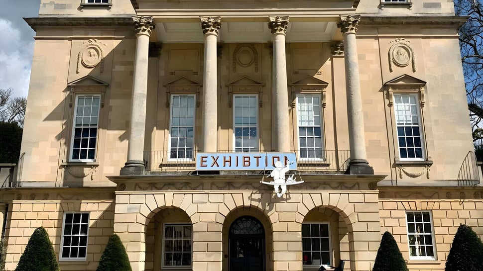 El edificio principal neoclásico de la Bath Academy está rodeado de árboles y se encuentra en una plaza pavimentada.