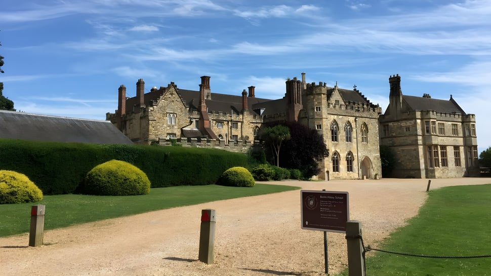 El castillo medieval en el terreno de la Battle Abbey School con césped cuidado y un camino de grava en primer plano.